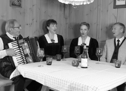 Vier Mitglieder des Rainer Quartetts beim gemeinsamen Singen an einem Tisch, eines davon mit Akkordeon.