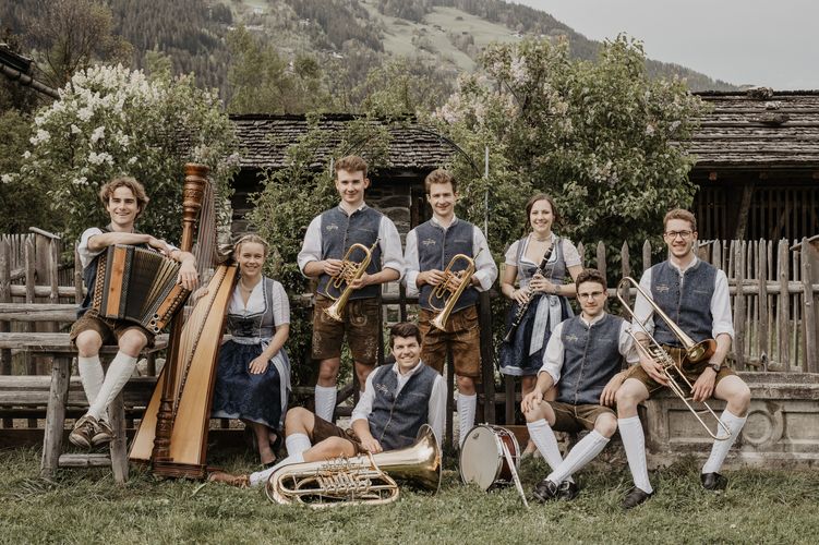 Die Musiker der Zillertaler Tanzlmusig posieren mit ihren Instrumenten vor einer rustikalen Holzhütte.